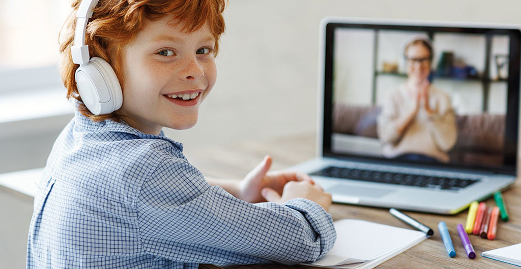 Smiling boy sitting in front of a laptop being tutored. 