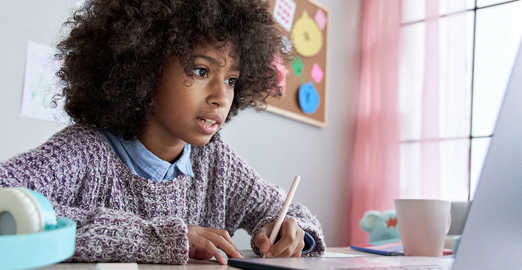 Girl sitting in front of a laptop with a pencil and paper in hand, getting help with school work.