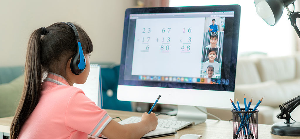 Girl with headphones on completing math homework on a desktop computer.